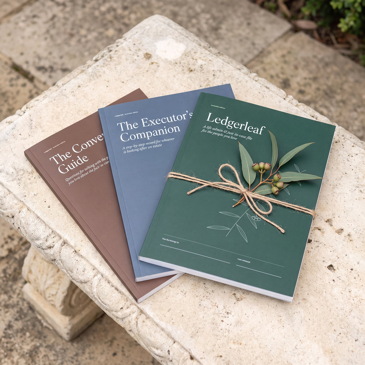The three Ledgerleaf record books tied with twine and a gum sprig on a stone bench